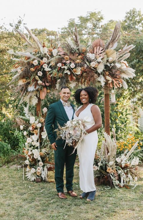 Savanna Inspired Flower and Dried Grass Wedding Ceremony Arch with a Stylish Bridal Jumpsuit